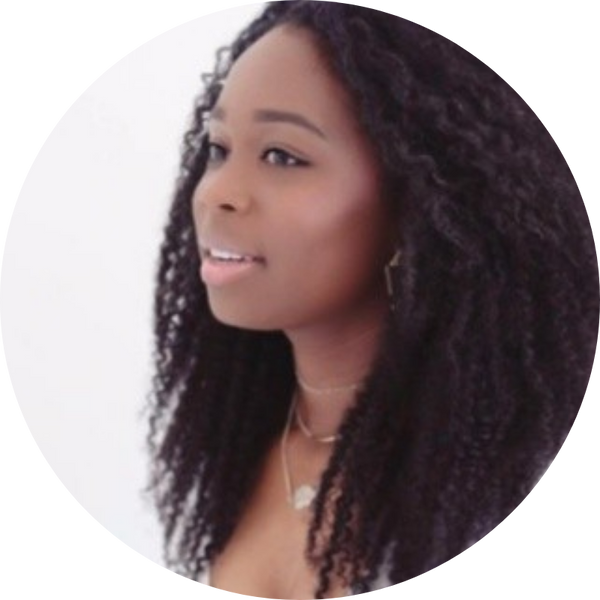 A woman with long, curly black hair smiling and looking to the side, dressed in a light top with layered necklaces against a white background.